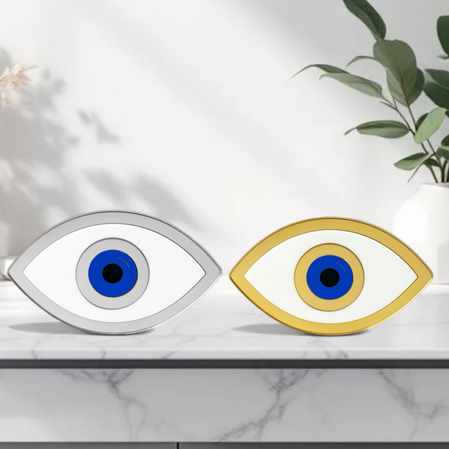 Two eye-shaped decorative items, one silver and one gold, on a marble surface with a plant in the background.