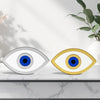 Two eye-shaped decorative items, one silver and one gold, on a marble surface with a plant in the background.