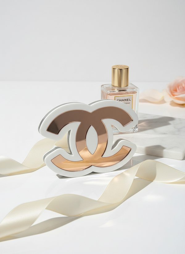 Επιτραπέζιο γούρι Double C από λευκό και ροζ χρυσό καθρέφτη, τοποθετημένο σε minimal λευκή επιφάνεια με άρωμα Chanel στο φόντο.