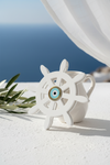 White plexiglass ship's wheel with a blue evil eye on a white surface with ocean view