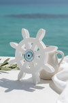 White ship's wheel decorative item on a white surface with a blue ocean background