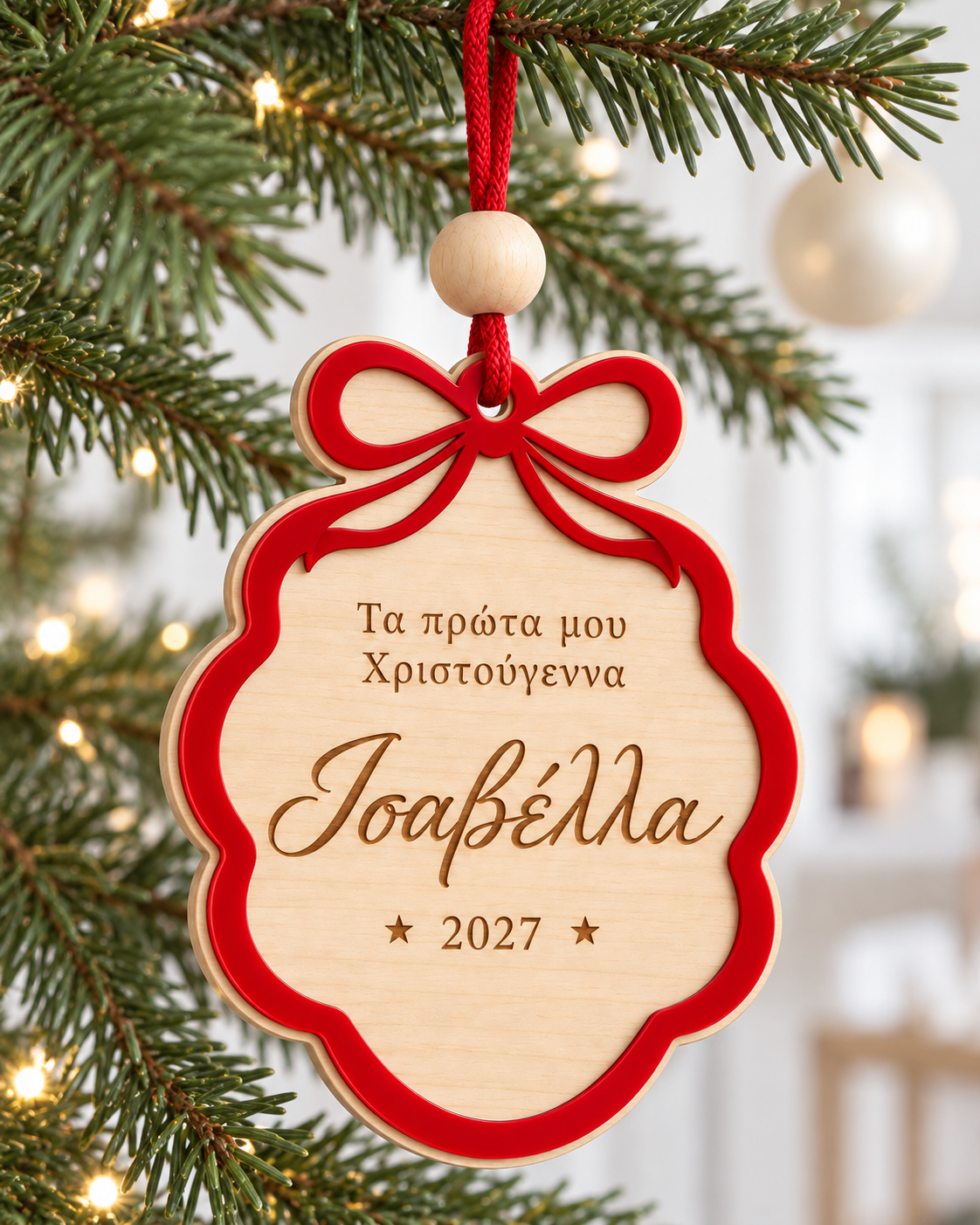Προσωποποιημένο στολίδι FIRST BOW με κόκκινο φιόγκο και το όνομα Ισαβέλλα, κρεμασμένο σε χριστουγεννιάτικο δέντρο σε φωτεινό Nordic σκηνικό – So Cute Cut.