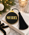 MERRY μαύρο και χρυσό χριστουγεννιάτικο γούρι μπάλα με μαύρη φούντα, πάνω σε λευκή επιφάνεια με χριστουγεννιάτικο έλατο, κερί και κομψή συσκευασία δώρου – So Cute Cut