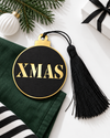 Μαύρο και χρυσό γούρι μπάλα XMAS με μαύρη φούντα πάνω σε πράσινο ύφασμα, με κλαδί έλατου, λευκή χριστουγεννιάτικη μπάλα και δώρο με μαύρη κορδέλα – So Cute Cut.