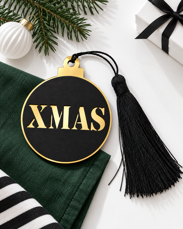Μαύρο και χρυσό γούρι μπάλα XMAS με μαύρη φούντα πάνω σε πράσινο ύφασμα, με κλαδί έλατου, λευκή χριστουγεννιάτικη μπάλα και δώρο με μαύρη κορδέλα – So Cute Cut.